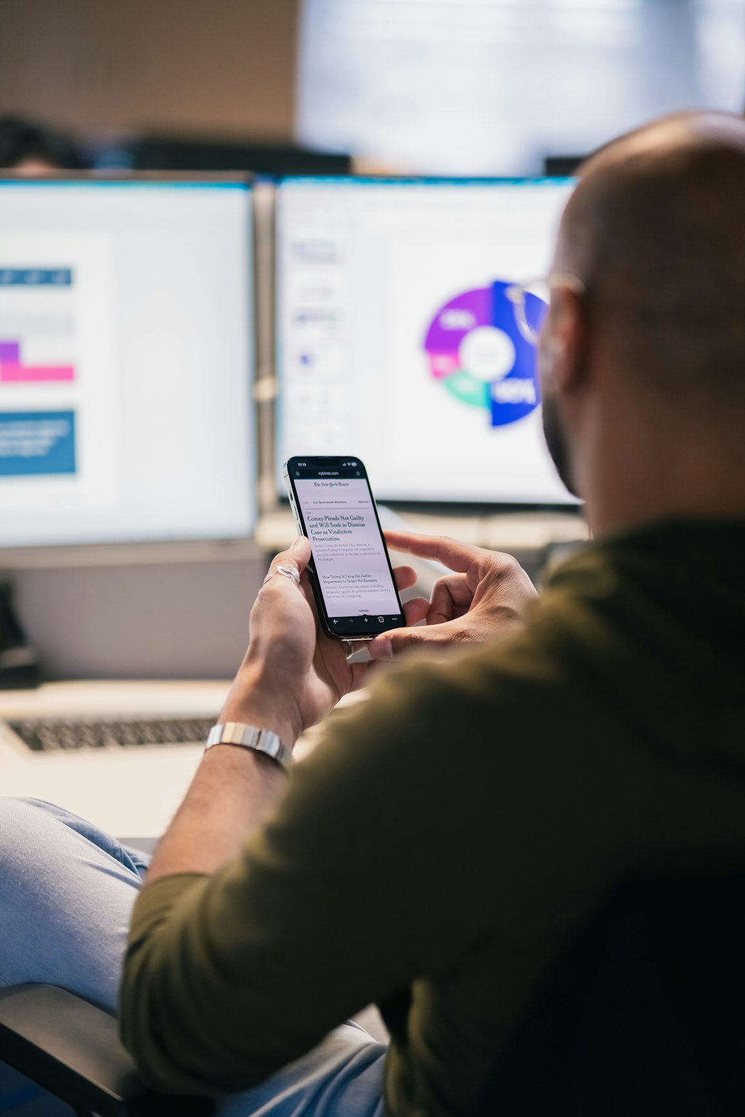 Man using smartphone in front of computer monitors